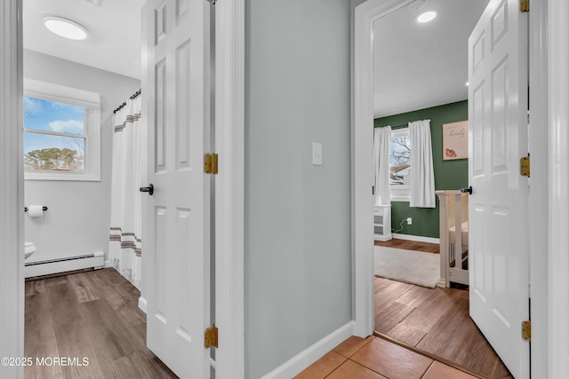 corridor featuring a wealth of natural light, wood finished floors, baseboards, and baseboard heating