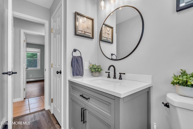 bathroom featuring toilet, vanity, a baseboard heating unit, and wood finished floors