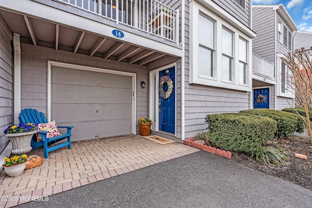 entrance to property featuring a garage, decorative driveway, and a balcony