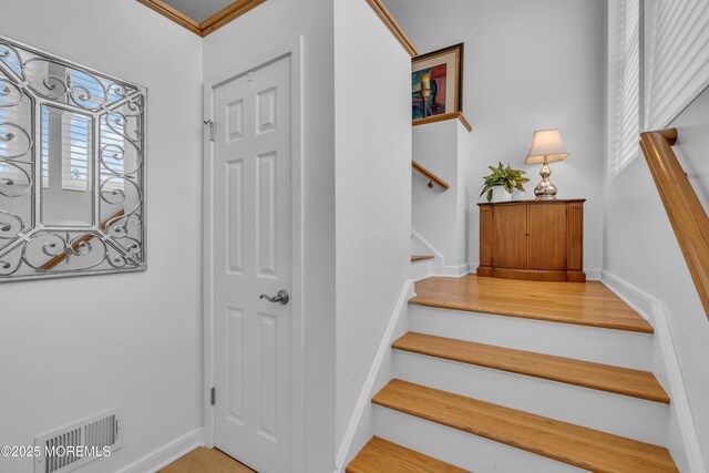 stairs with visible vents, baseboards, and crown molding