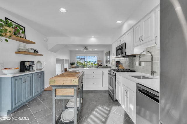 kitchen featuring open shelves, a peninsula, a sink, stainless steel appliances, and backsplash