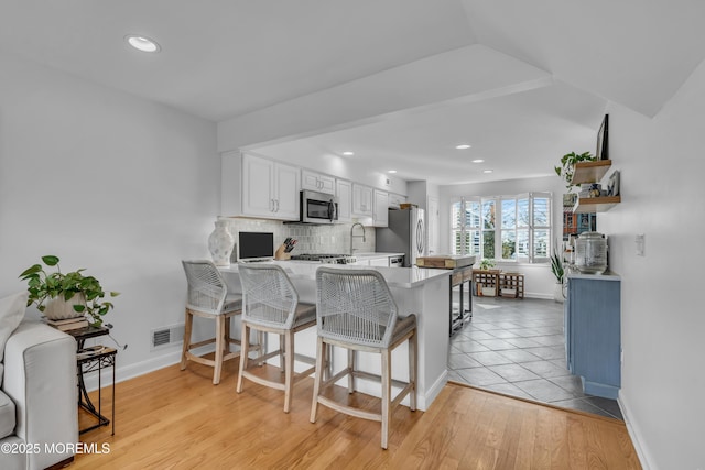 kitchen with a sink, decorative backsplash, light countertops, stainless steel appliances, and white cabinetry