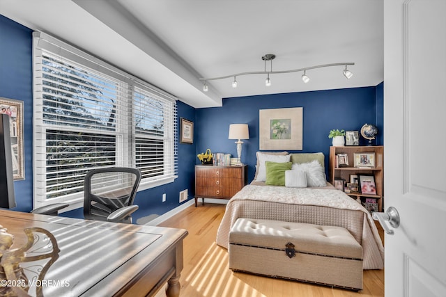 bedroom featuring baseboards, light wood-style floors, and rail lighting