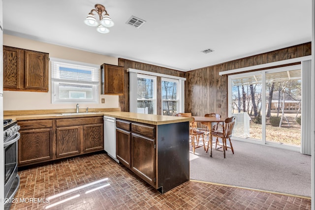 kitchen featuring light countertops, a peninsula, white dishwasher, stainless steel range, and a sink