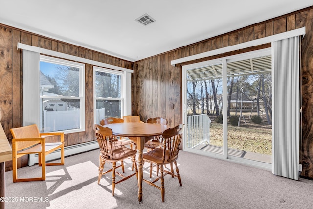 carpeted dining space featuring visible vents, wood walls, and a baseboard heating unit