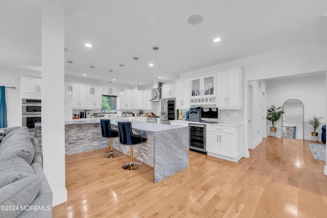 kitchen with a kitchen bar, wine cooler, arched walkways, appliances with stainless steel finishes, and white cabinets