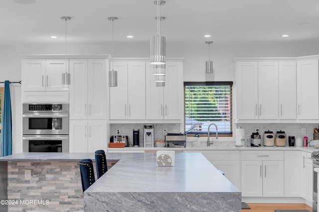 kitchen with decorative light fixtures, decorative backsplash, appliances with stainless steel finishes, white cabinetry, and a sink