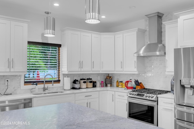 kitchen featuring wall chimney range hood, light countertops, appliances with stainless steel finishes, white cabinets, and a sink