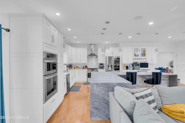 kitchen featuring light wood-type flooring, open floor plan, white cabinetry, stainless steel appliances, and wall chimney range hood