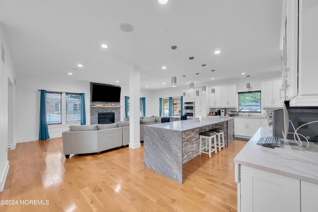 kitchen with a stone fireplace, light wood-style floors, white cabinetry, and stainless steel double oven