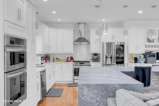 kitchen with light wood-style floors, tasteful backsplash, appliances with stainless steel finishes, and wall chimney exhaust hood