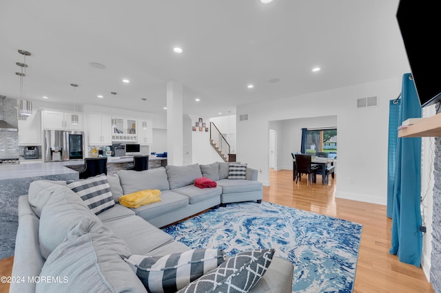 living room with visible vents, light wood finished floors, baseboards, recessed lighting, and stairs