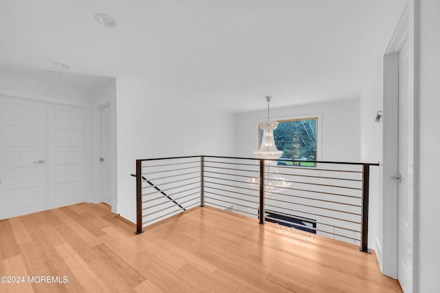 corridor featuring an upstairs landing, an inviting chandelier, and wood finished floors