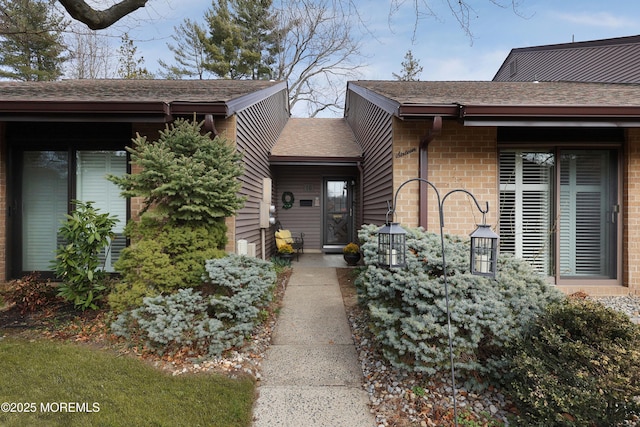 doorway to property with brick siding and a shingled roof