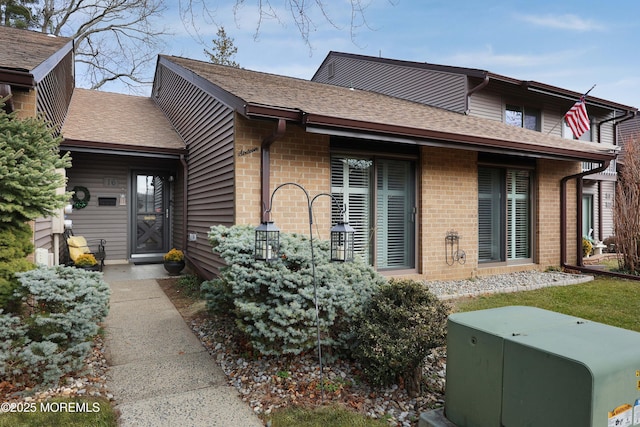 back of house featuring brick siding and a shingled roof