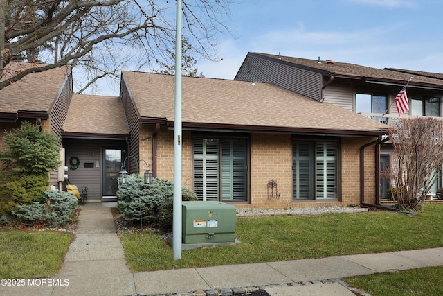 view of property with brick siding, a front lawn, and roof with shingles