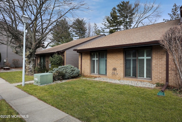 exterior space with a yard, brick siding, and roof with shingles