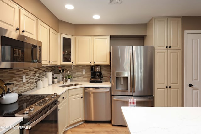 kitchen with decorative backsplash, light wood-style flooring, appliances with stainless steel finishes, and a sink