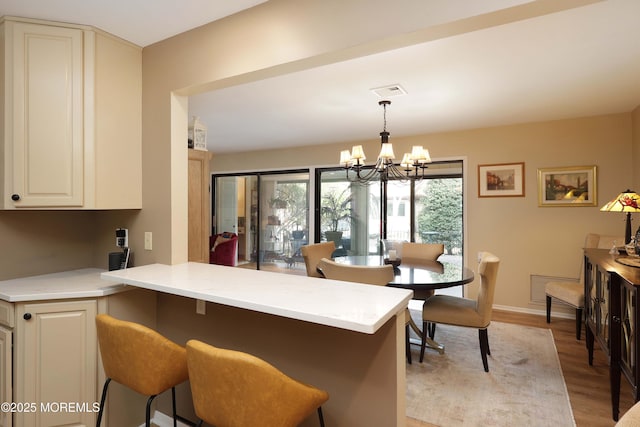 kitchen with visible vents, a notable chandelier, a kitchen breakfast bar, light wood-style floors, and a peninsula