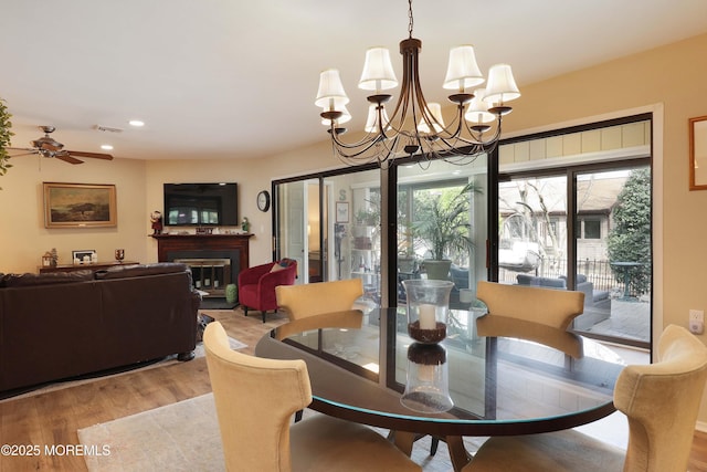 dining area featuring light wood-type flooring, visible vents, ceiling fan with notable chandelier, a glass covered fireplace, and recessed lighting