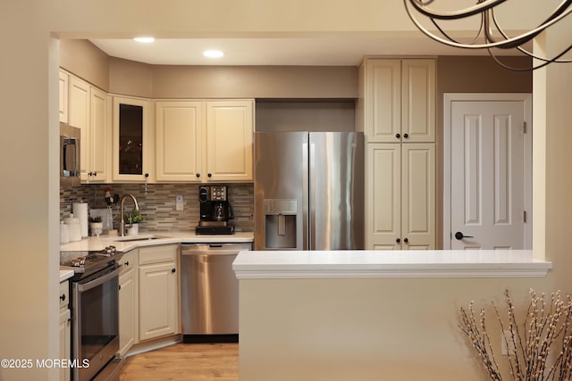 kitchen with a sink, light countertops, appliances with stainless steel finishes, tasteful backsplash, and light wood-type flooring