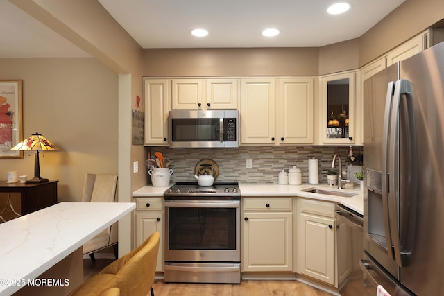 kitchen featuring glass insert cabinets, decorative backsplash, recessed lighting, appliances with stainless steel finishes, and a sink