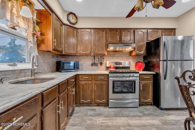 kitchen with under cabinet range hood, decorative backsplash, appliances with stainless steel finishes, and a sink