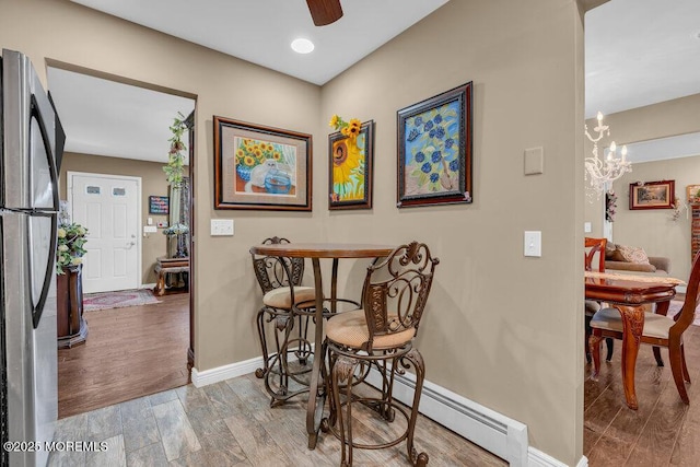 dining area featuring ceiling fan with notable chandelier, wood finished floors, baseboards, and baseboard heating