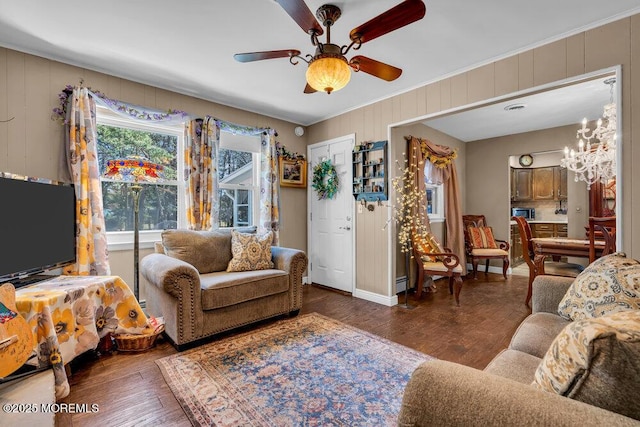 living area with ceiling fan with notable chandelier, crown molding, baseboards, and wood finished floors