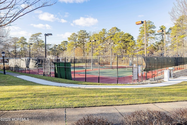 view of tennis court featuring a lawn and fence