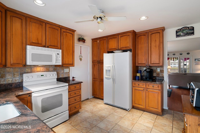 kitchen with dark countertops, decorative backsplash, brown cabinetry, white appliances, and a ceiling fan