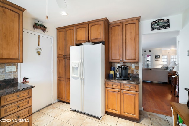 kitchen with brown cabinetry, dark stone counters, tasteful backsplash, and white fridge with ice dispenser