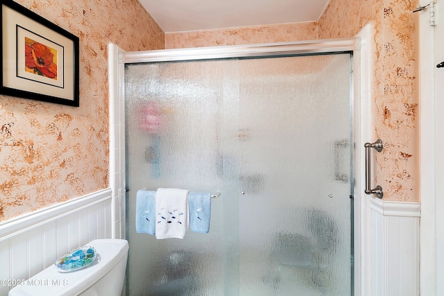 full bathroom featuring toilet, a stall shower, wainscoting, and wallpapered walls