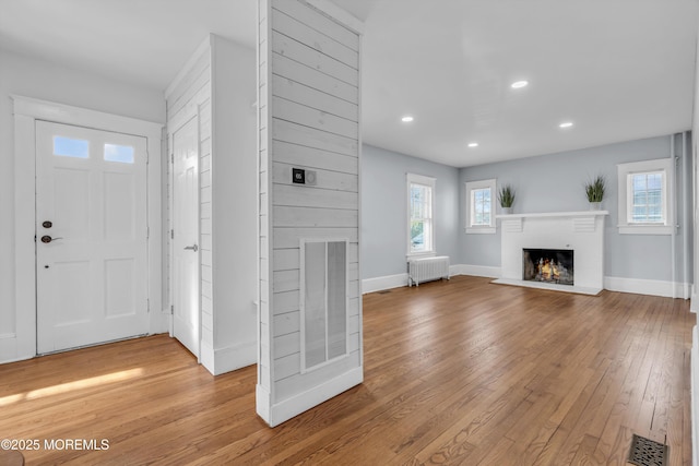 foyer entrance with hardwood / wood-style floors, radiator heating unit, visible vents, and a warm lit fireplace