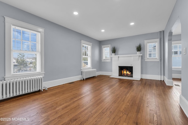 unfurnished living room with baseboards, radiator, a brick fireplace, and hardwood / wood-style flooring