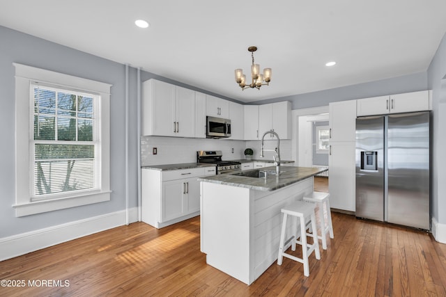 kitchen with backsplash, white cabinetry, stainless steel appliances, light wood-style floors, and a chandelier