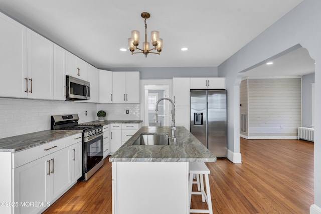 kitchen featuring a sink, appliances with stainless steel finishes, wood finished floors, and radiator heating unit