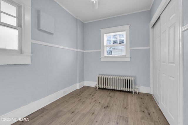 empty room featuring ornamental molding, radiator, baseboards, and wood finished floors