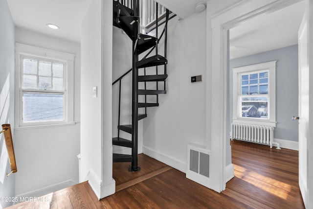 stairway with visible vents, plenty of natural light, radiator heating unit, and wood-type flooring