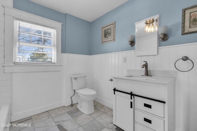 bathroom featuring toilet, marble finish floor, wainscoting, a bathtub, and vanity