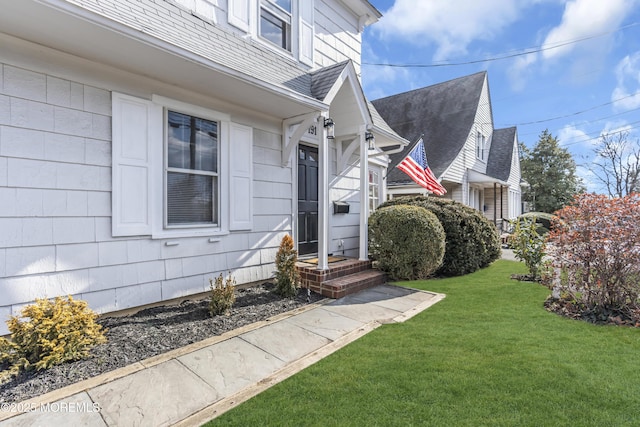 entrance to property with a yard and a shingled roof