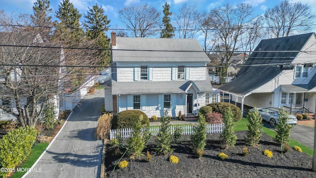 view of front facade with a fenced front yard, driveway, a chimney, and a shingled roof