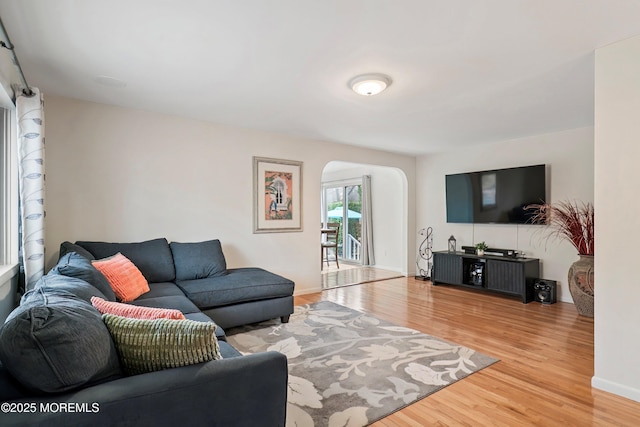 living room featuring arched walkways, light wood-style flooring, and baseboards