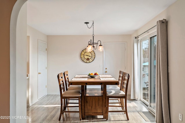 dining space with a chandelier, arched walkways, baseboards, and light wood-style floors