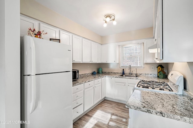 kitchen featuring white appliances, light stone countertops, a sink, light wood-style floors, and white cabinetry