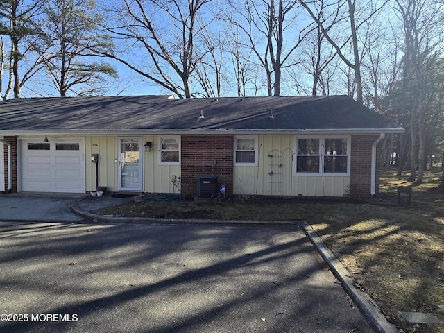 single story home featuring brick siding, an attached garage, central AC unit, and board and batten siding