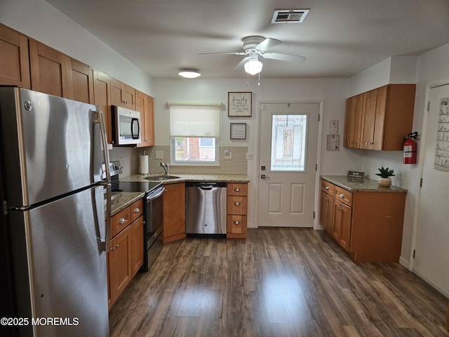 kitchen featuring brown cabinetry, visible vents, dark wood finished floors, ceiling fan, and appliances with stainless steel finishes