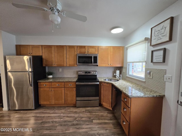 kitchen featuring dark wood-type flooring, light stone countertops, brown cabinets, stainless steel appliances, and a sink