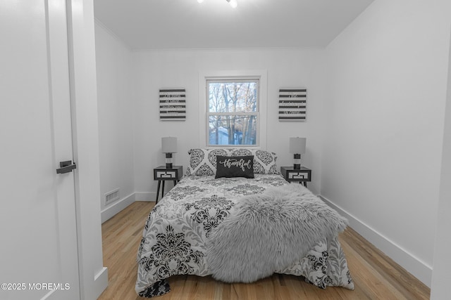 bedroom with light wood-type flooring, visible vents, baseboards, and crown molding