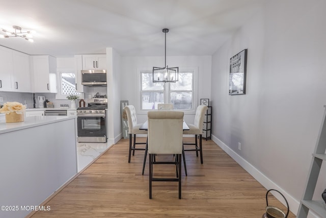 dining space with light wood-style floors, baseboards, and a notable chandelier